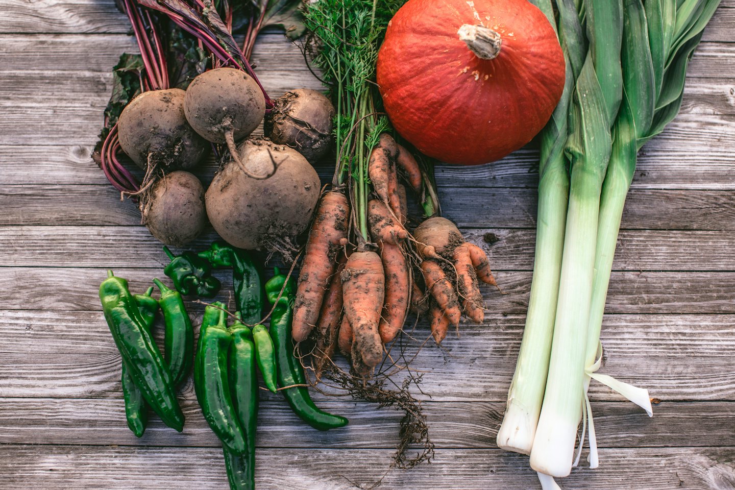 Assortimento di barbabietole, carote, peperoni, porri e zucca non lavati su legno.